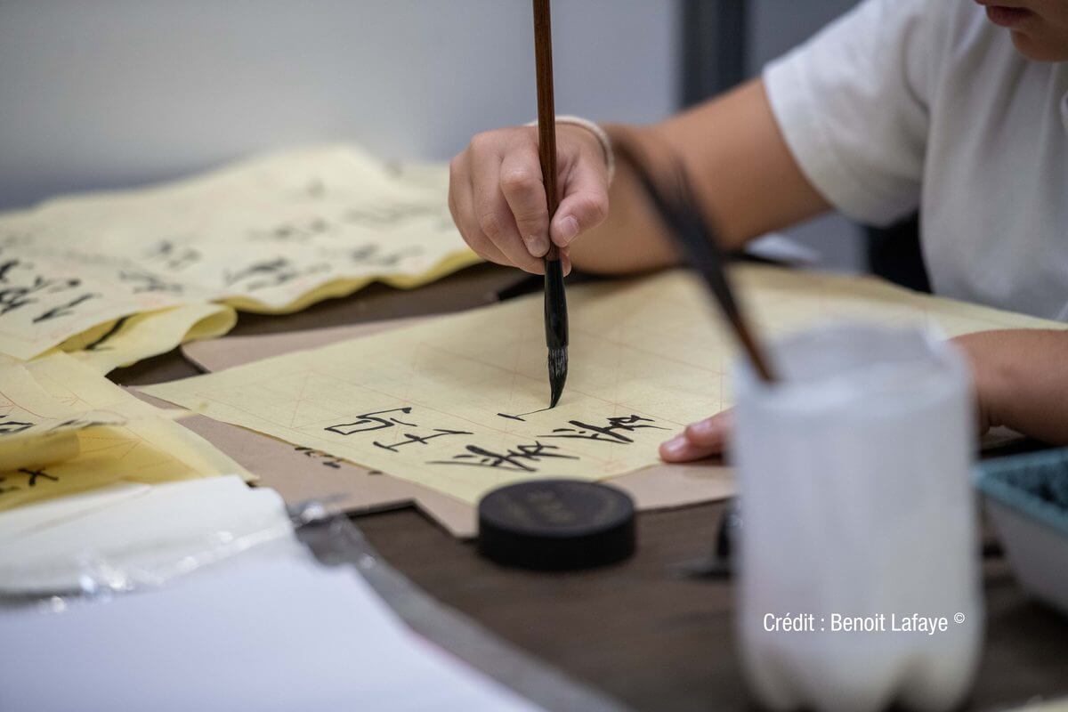 Main qui trace des caractères asiatiques au pinceau lors d'un atelier de calligraphie
