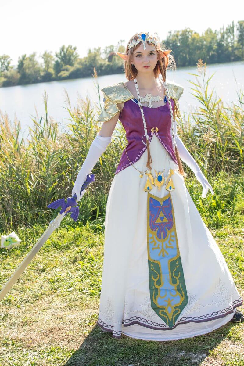 Cosplayeuse en princesse Zelda avec une épée, au bord d'un lac