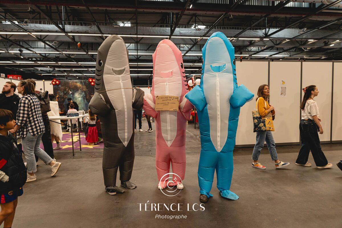 Trois visiteurs en costumes gonflables de requins dans les allées d'Animasia
