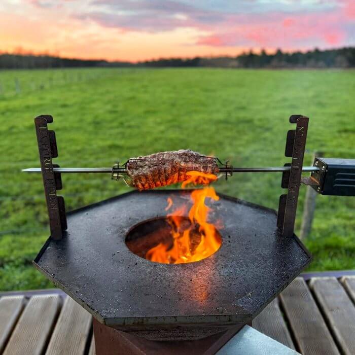 Rôti sur tourne-broche au-dessus du feu d'un brasero au coucher du soleil