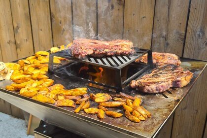 Côtes de bœuf, potatoes et camembert rôti sur la plancha d'un brasero carré PFC, flamme au centre