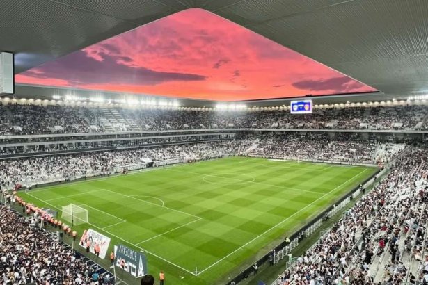 Le Stade Atlantique de Bordeaux plein, pelouse et tribunes sous un ciel rose au coucher du soleil