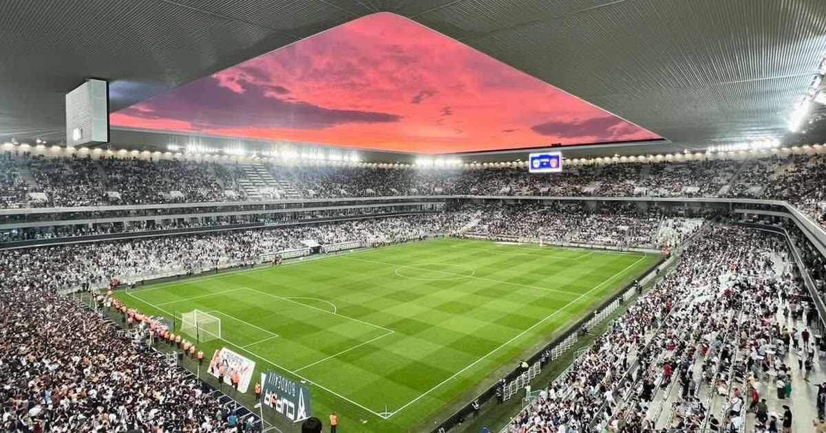 Le Stade Atlantique de Bordeaux plein, pelouse et tribunes sous un ciel rose au coucher du soleil