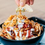 Bol de nachos garnis de viande, tomates, oignons frits et sauce blanche, avec une chips trempée dans le guacamole, chez Nachos à Mérignac
