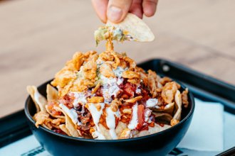 Bol de nachos garnis de viande, tomates, oignons frits et sauce blanche, avec une chips trempée dans le guacamole, chez Nachos à Mérignac