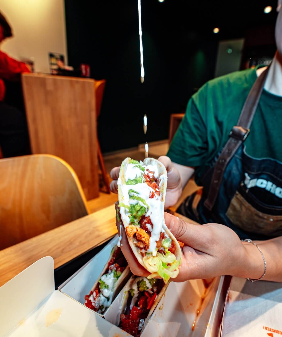 Taco garni de viande, salade et sauce tenu à la main, chez Nachos à Mérignac
